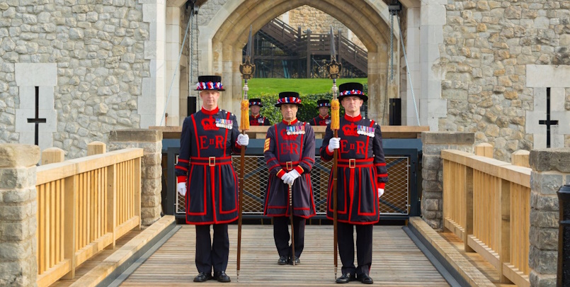 “Three Beefeater guards dressed in traditional red and black tunics standing at the entrance to the Tower of London.”