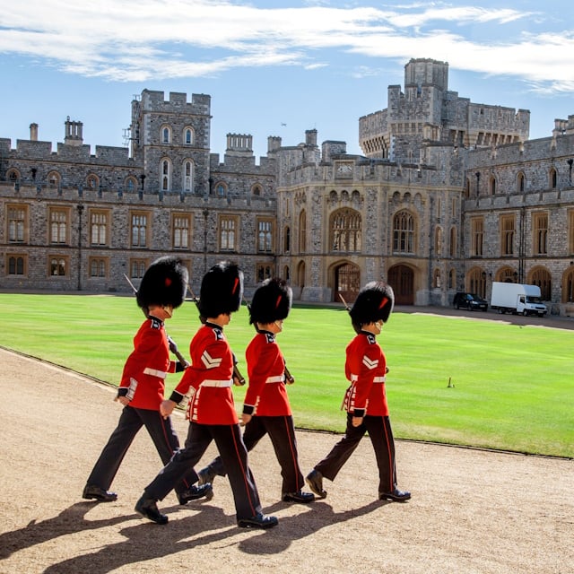 “Marching Guardsmen in red tunics and bearskin hats in the inner courtyard at Windsor Castle during the Changing of the Guard.”